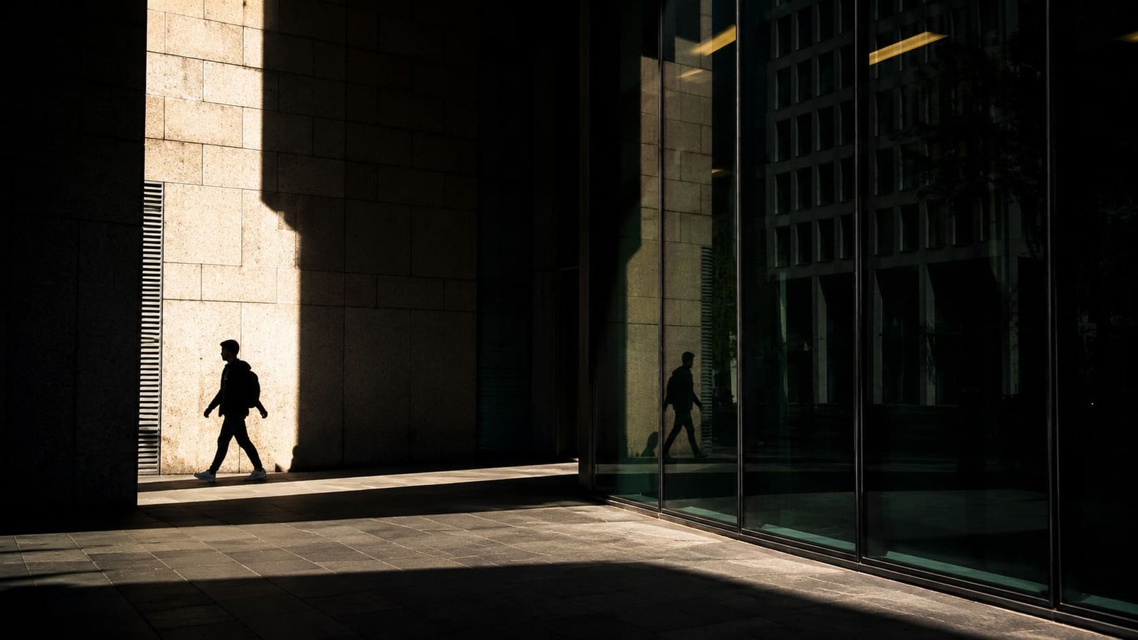 Área urbana com feixe da luz do sol sobre prédio com sombra de uma pessoa à esquerda e área espelhada à direita ilustrando artigo Reflexos e sombras na fotografia.