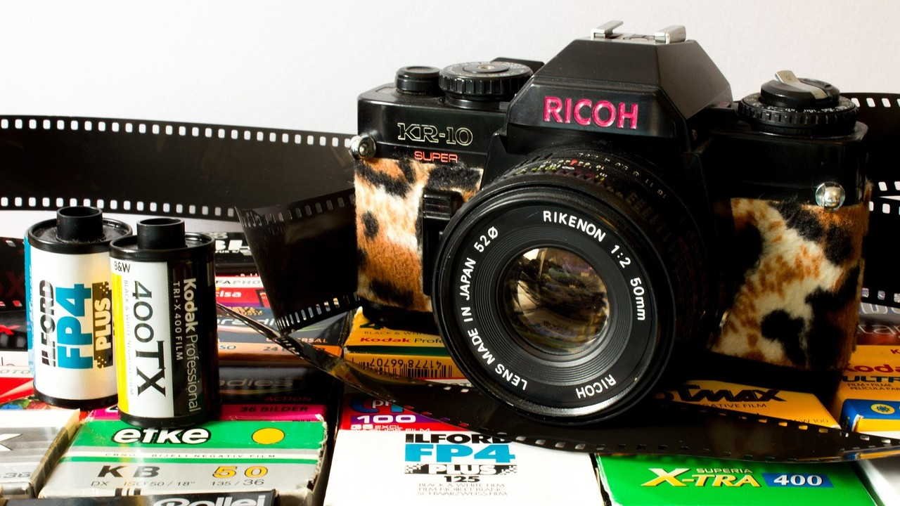 Câmera Ricoh sobre a mesa com rolos de filmes à esquerda, ilustrando artigo A Ricoh ainda fabrica câmeras?